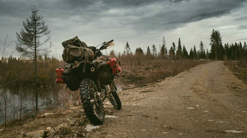 moto com bagagem, estacionada em uma estrada de terra, próximo a um rio