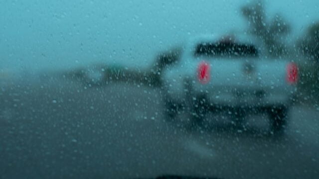 A foto mostra um vidro embaçado e com gotas de chuva e a frente uma caminhonete branca 